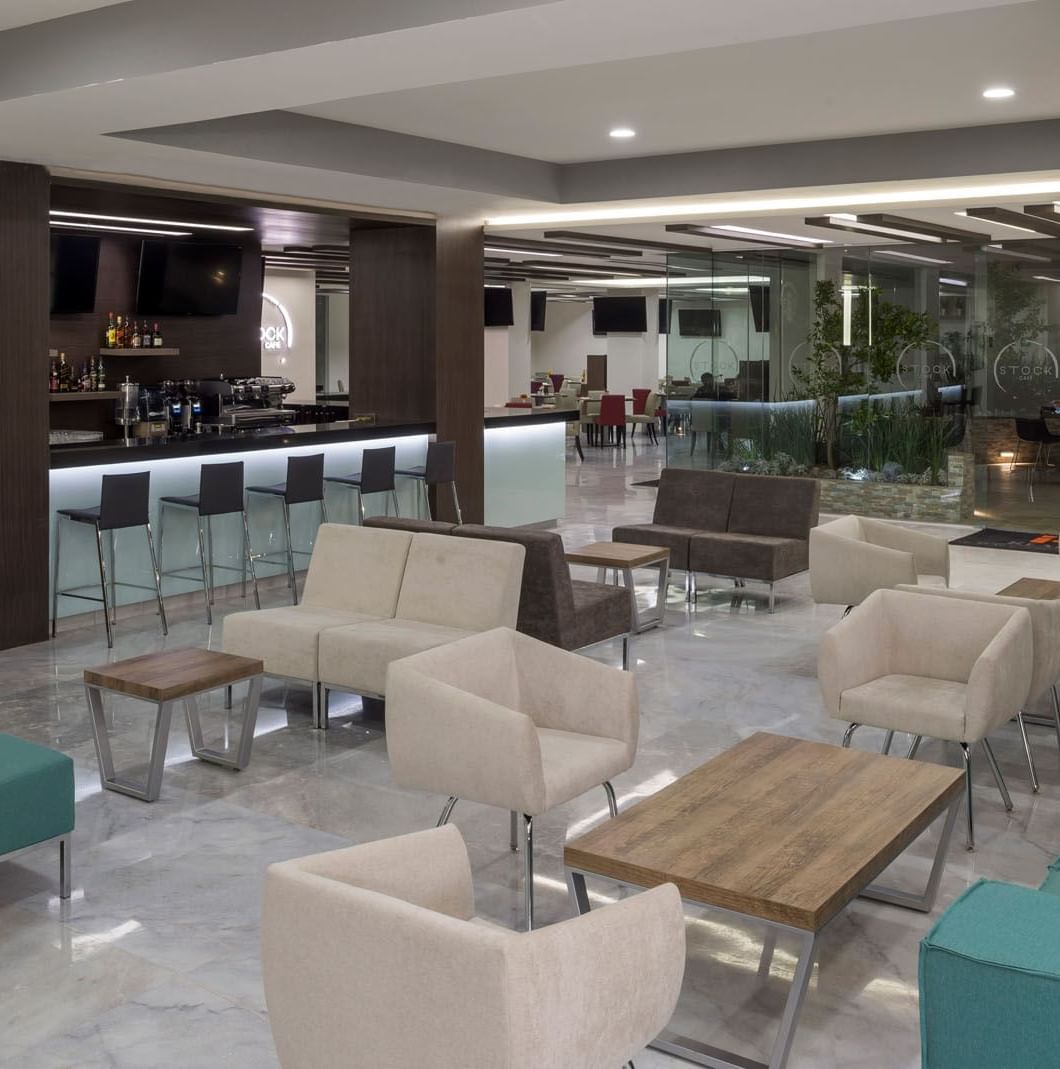 Lobby Bar at Real Inn Celaya with teal sofas, modern light fixtures, and a well-stocked spirit shelf