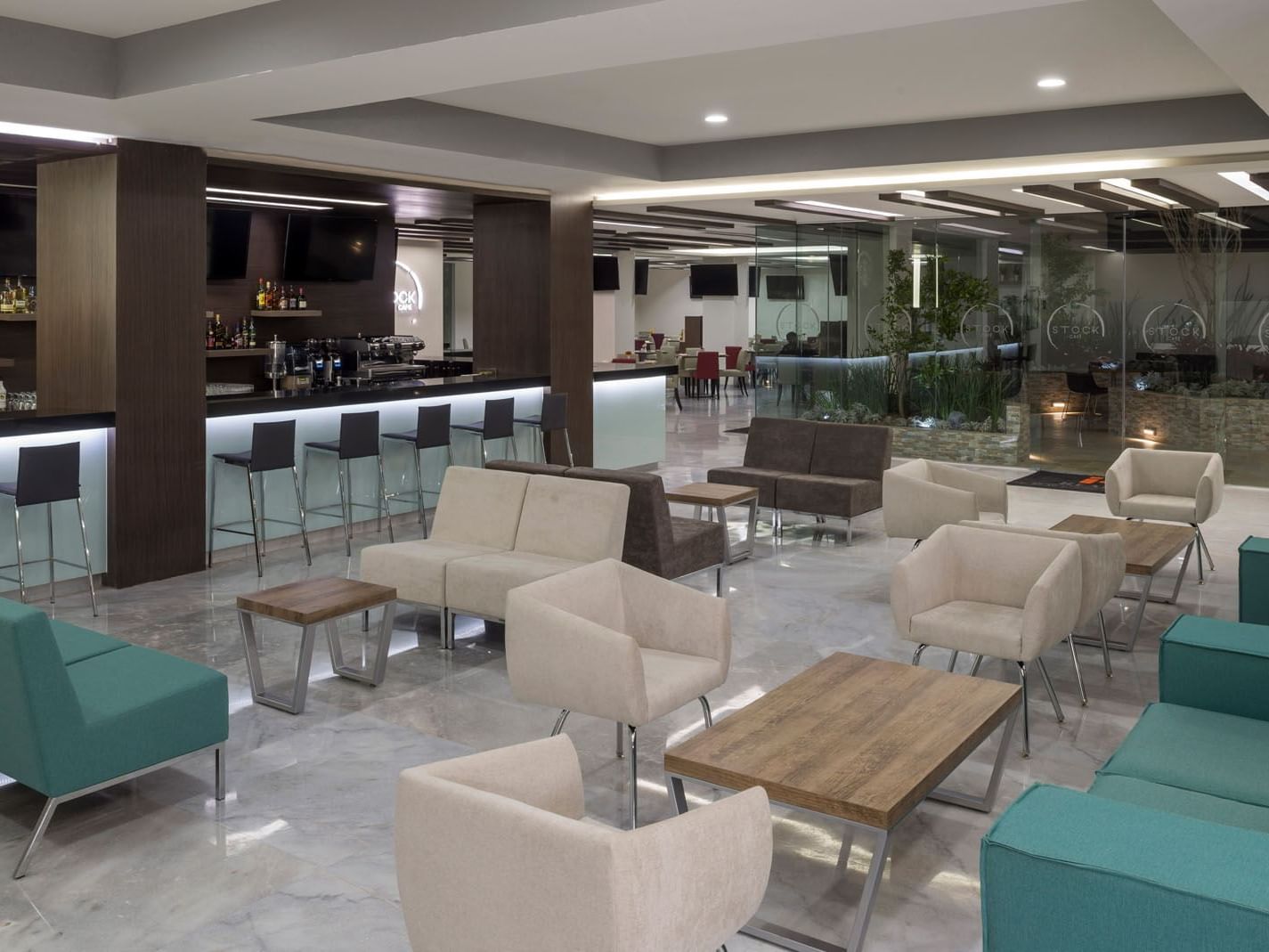 Lobby Bar at Real Inn Celaya with teal sofas, modern light fixtures, and a well-stocked spirit shelf