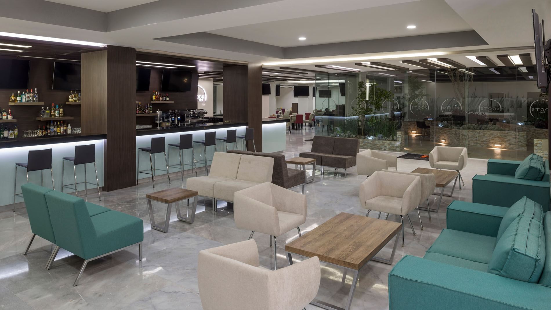 Lobby Bar at Real Inn Celaya with teal sofas, modern light fixtures, and a well-stocked spirit shelf