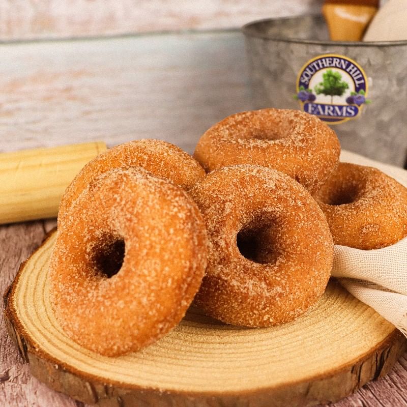 A stack of cinnamon sugar donuts on a sliced wooden display with a Southern Hill Farms bucket in the background.