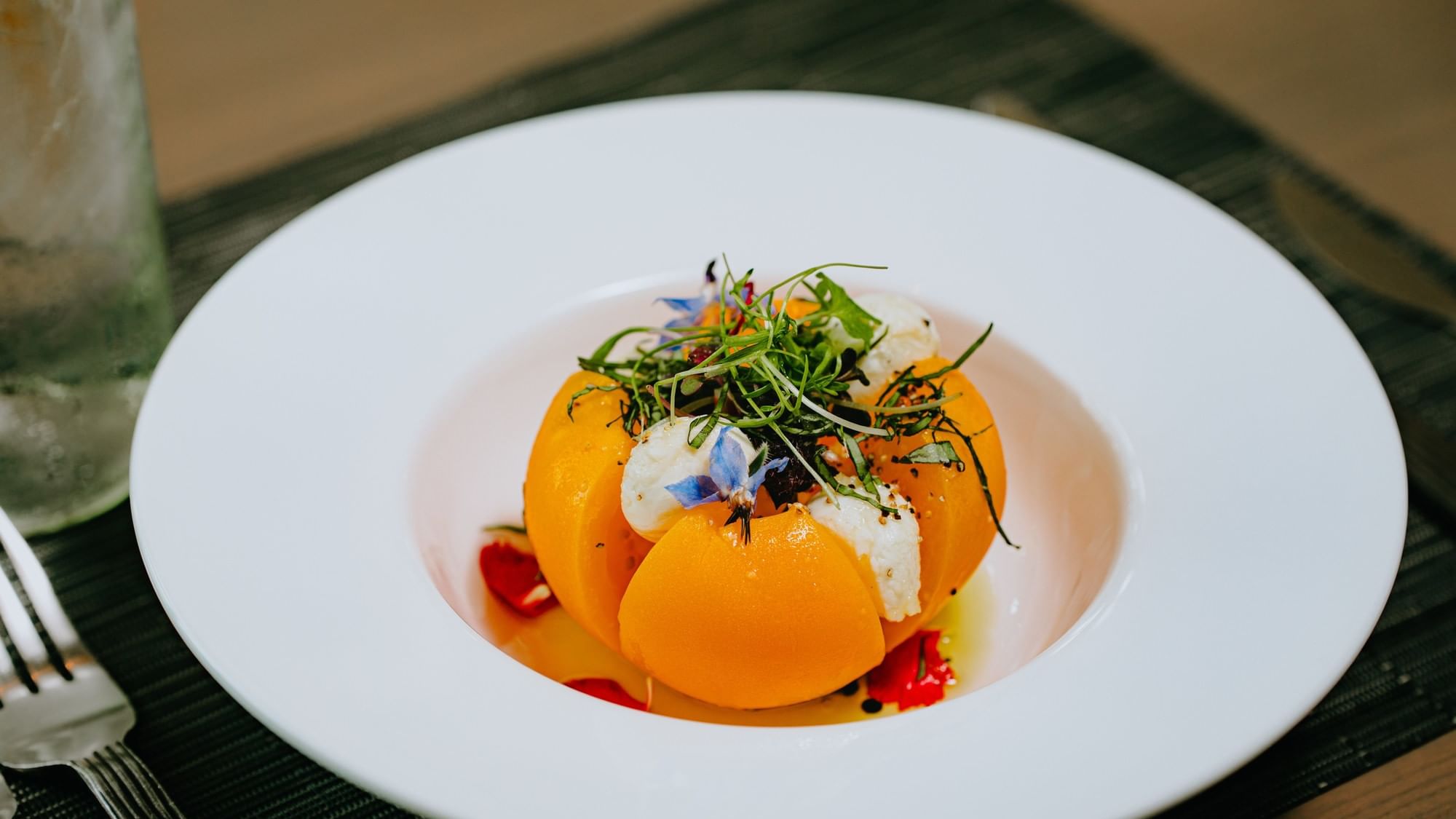 White plate with orange slices, herbs, and garnishes on a green placemat with a fork and a glass.