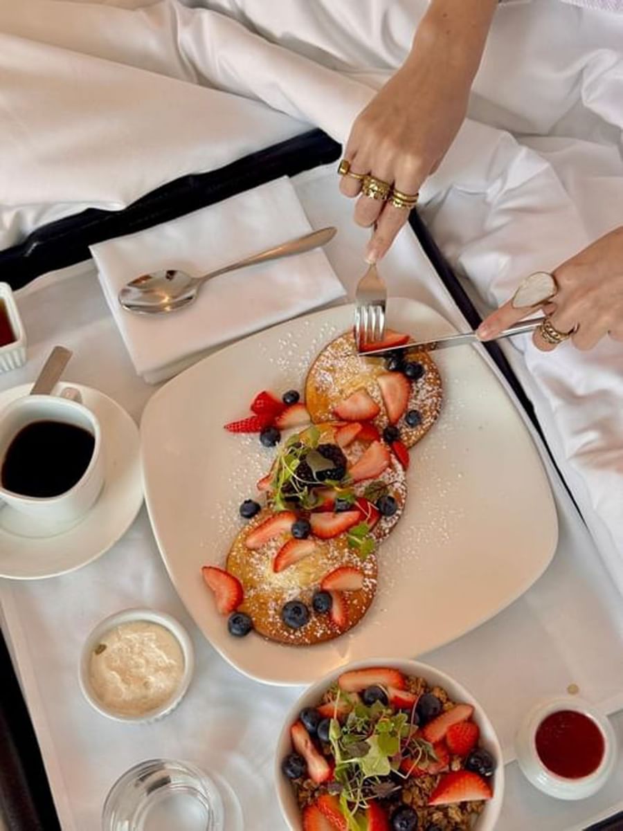 Pancakes topped with berries and sugar by a coffee cup and silverware at Warwick Le Crystal Montreal