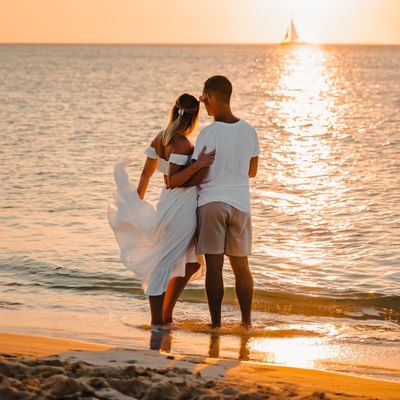 Couple embraces while admiring a vibrant ocean sunset near Amsterdam Manor Beach Resort