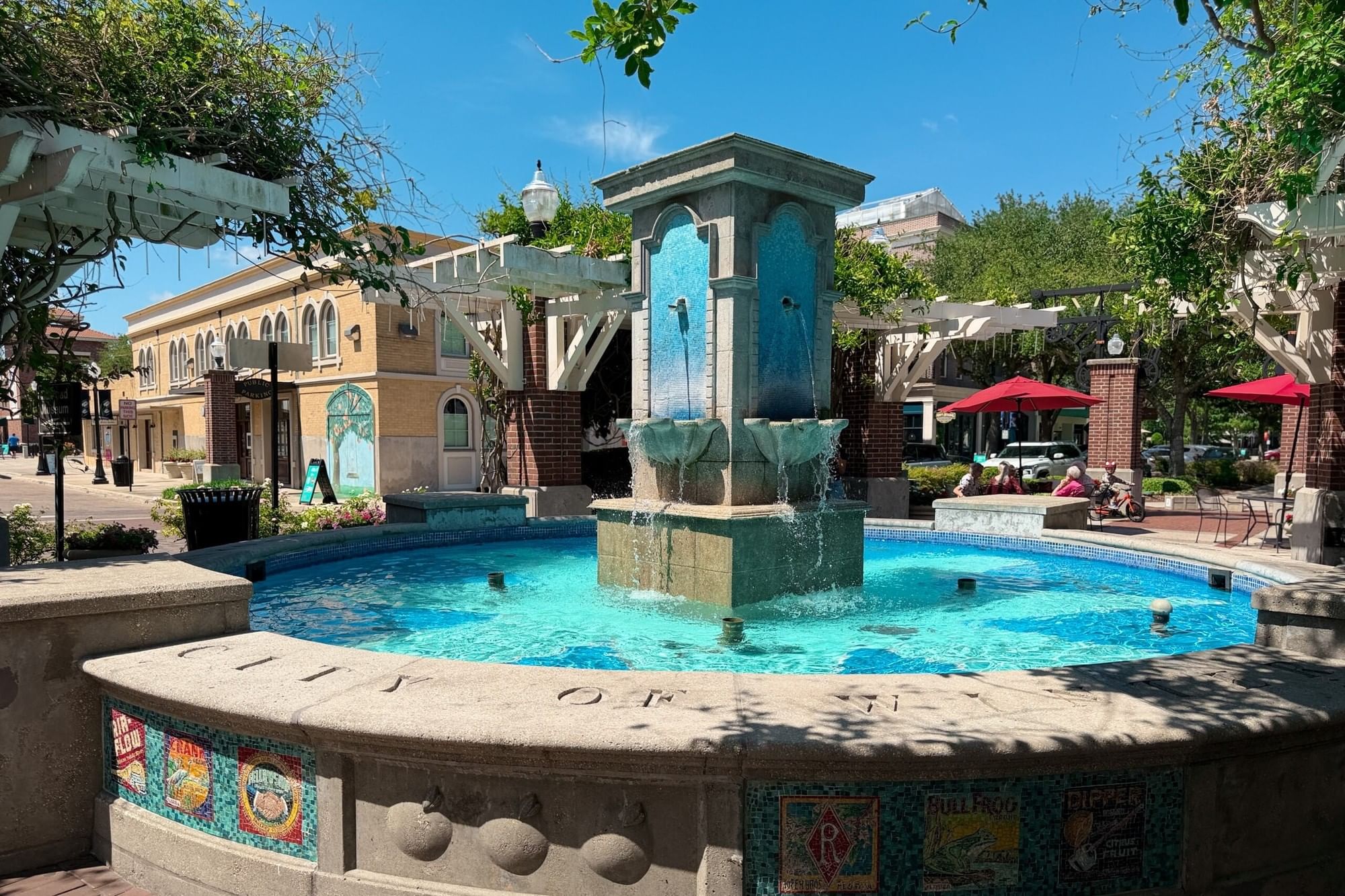 A crystal blue mosaic fountain surrounded by pergolas draped in greenery and red umbrellas in the heart of Winter Garden.