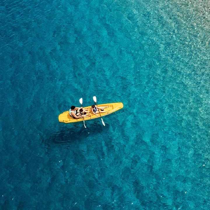 Due persone in un kayak giallo con due pagaie, visti dall'alto in acque blu.