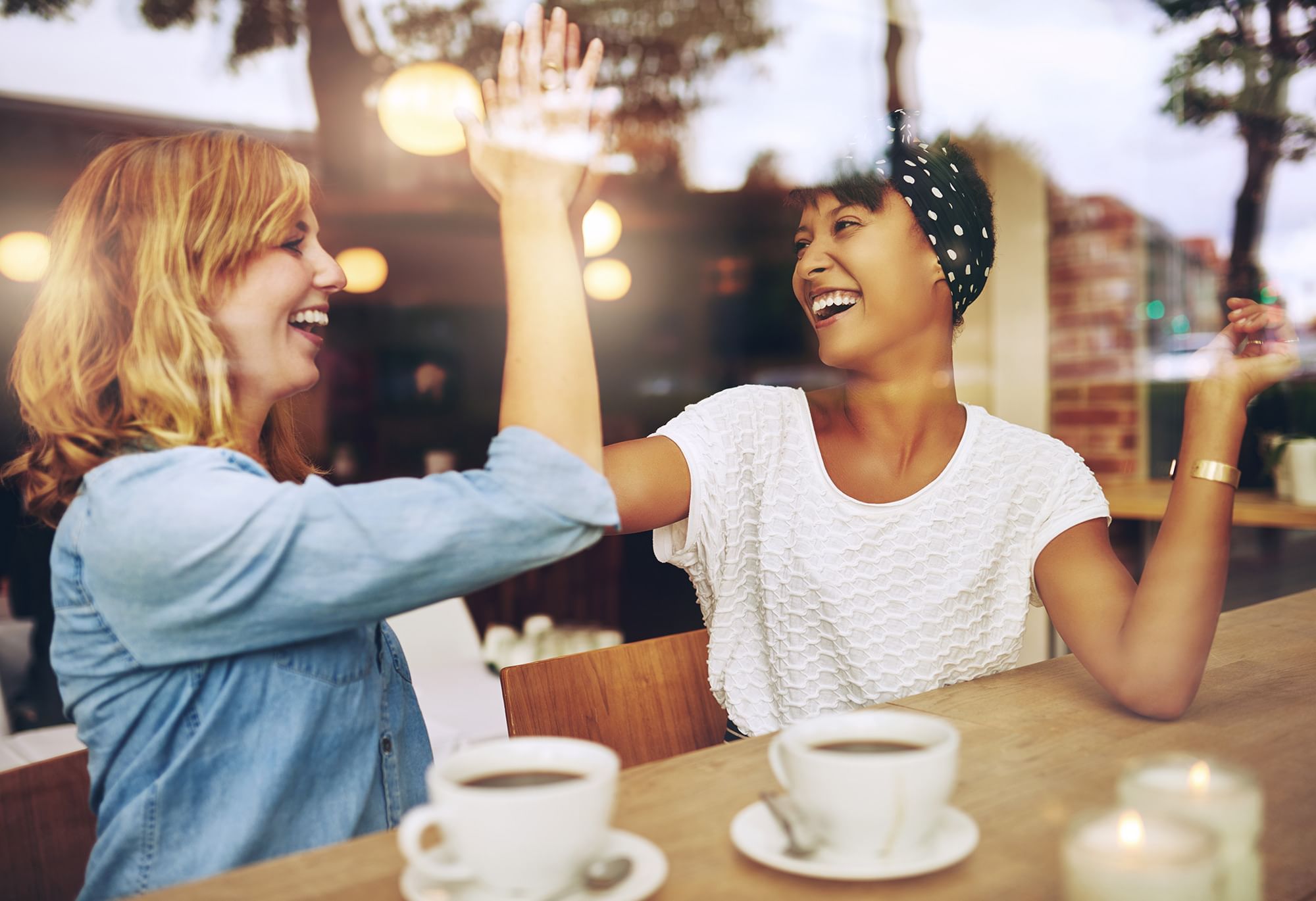 Two women high-fiving and drinking coffee at café