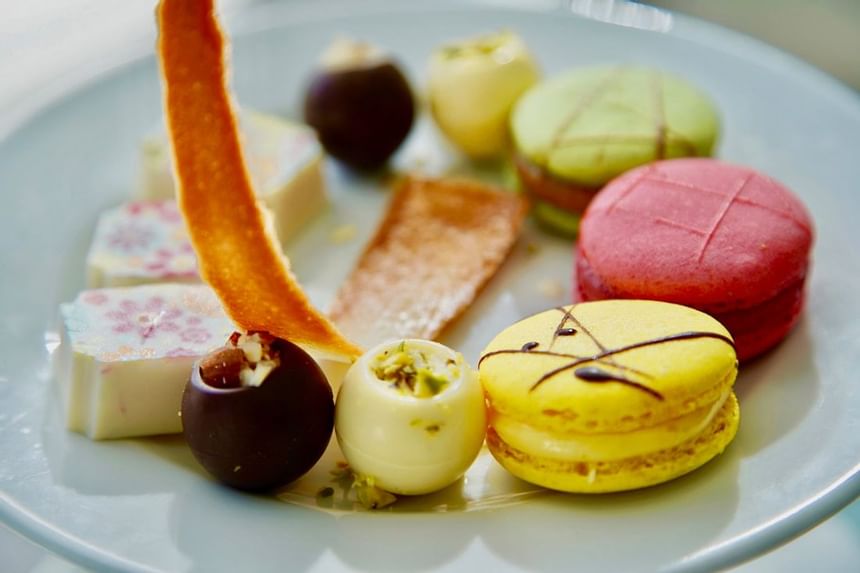 Colorful macarons and chocolate truffles served on a white dessert plate at The Abidah Hotel by Accra