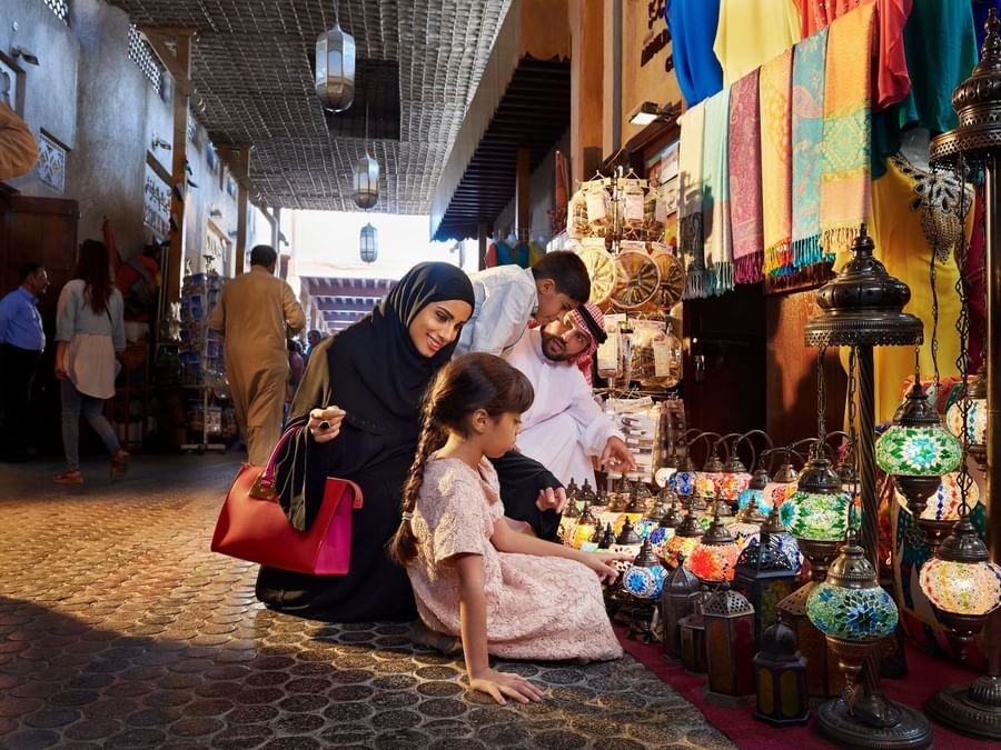 Individuals examining colorful lamps at a vibrant market stall near DAMAC Hotels & Resorts