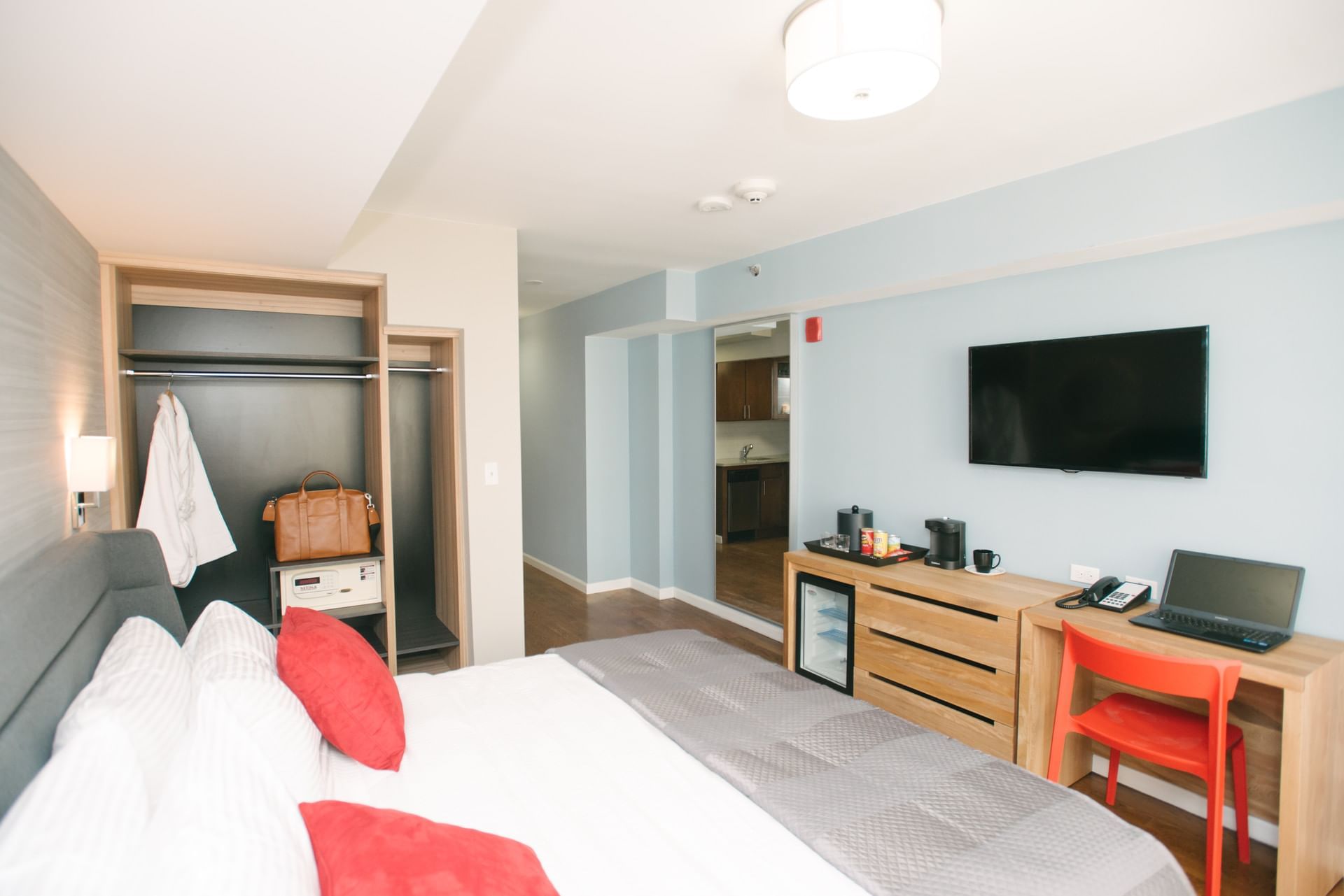 A hotel room with a king-sized bed, desk, TV, mini-fridge, and closet.