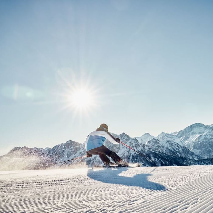 Skier carving a turn on a snowy mountain slope with sun shining brightly at Falkensteiner Group