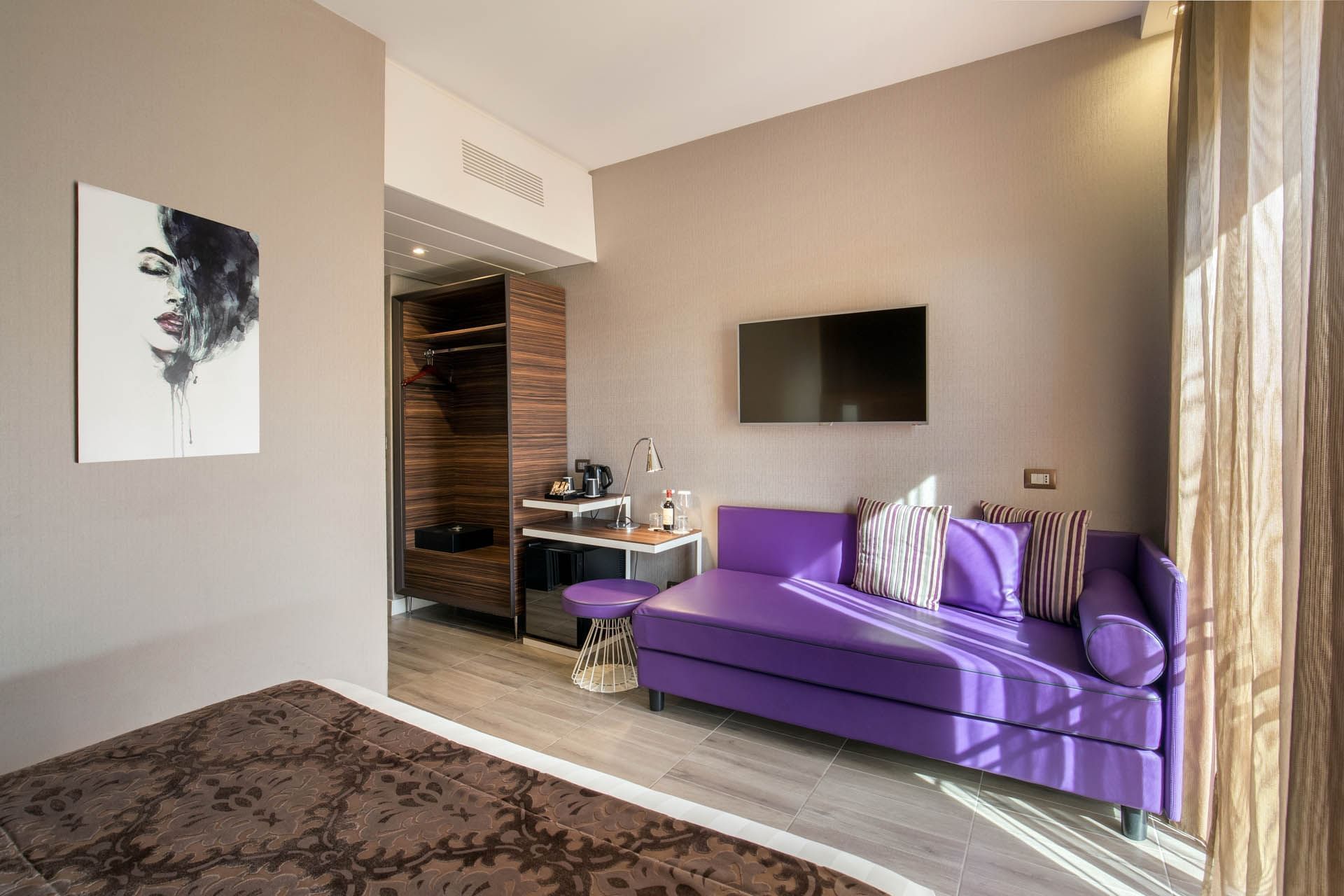 Deluxe Room featuring a purple couch, TV, a small table with refreshments, and elegant decor at The Republic Hotel