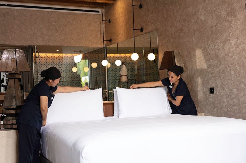 Two staff members arranging pillows on a bed in a room at Live Aqua Resorts and Residence Club