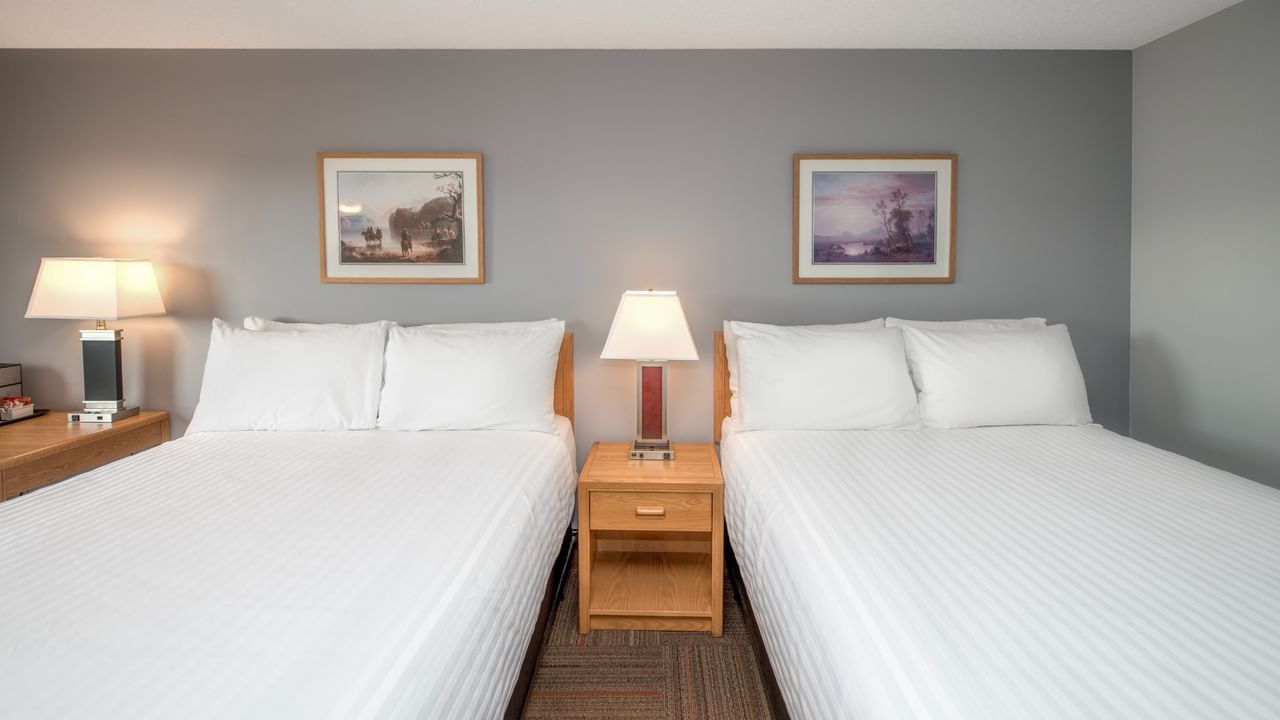 Two beds with white linens, bedside lamps, and framed artwork on gray walls.