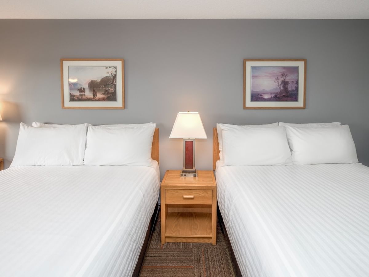 Two beds with white bedding and pillows, nightstands with lamps, and framed wall art.