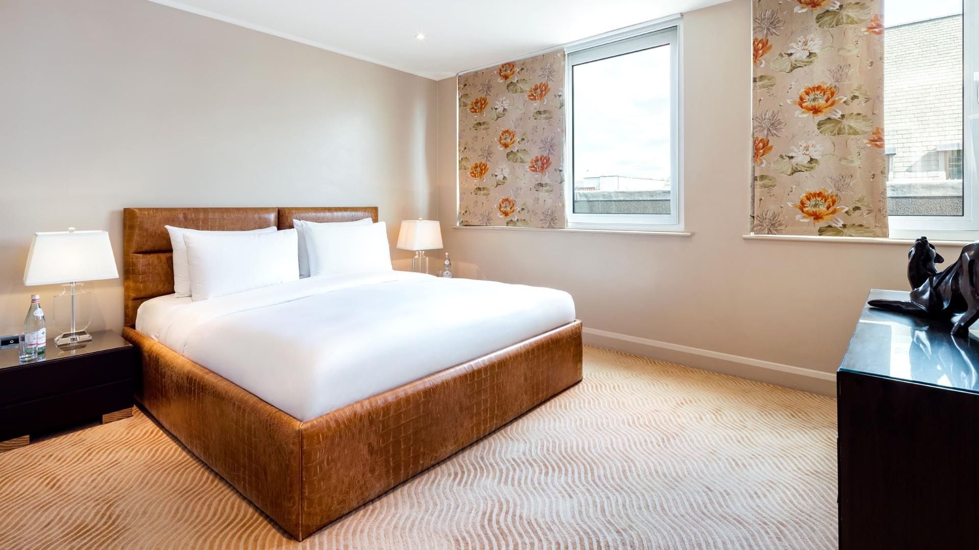 Elegant bedroom in the Saffron Suite at The May Fair Hotel London, featuring a large bed with bedside lamps, and windows