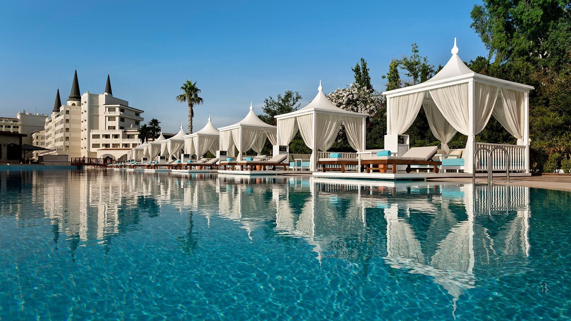 Sun loungers arranged under the shades of huts by the pool outdoors at Titanic Mardan Palace