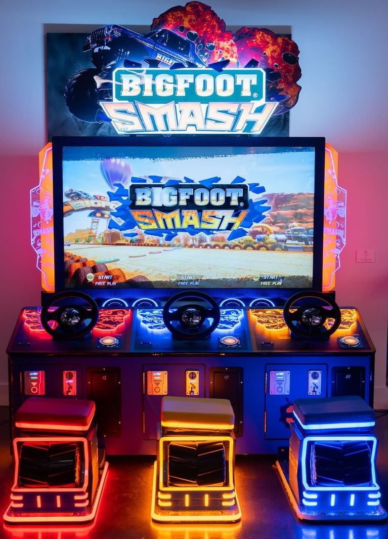 Three neon monster truck seats lined up under a Bigfoot Smash game screen and lit sign at Hotel X Toronto