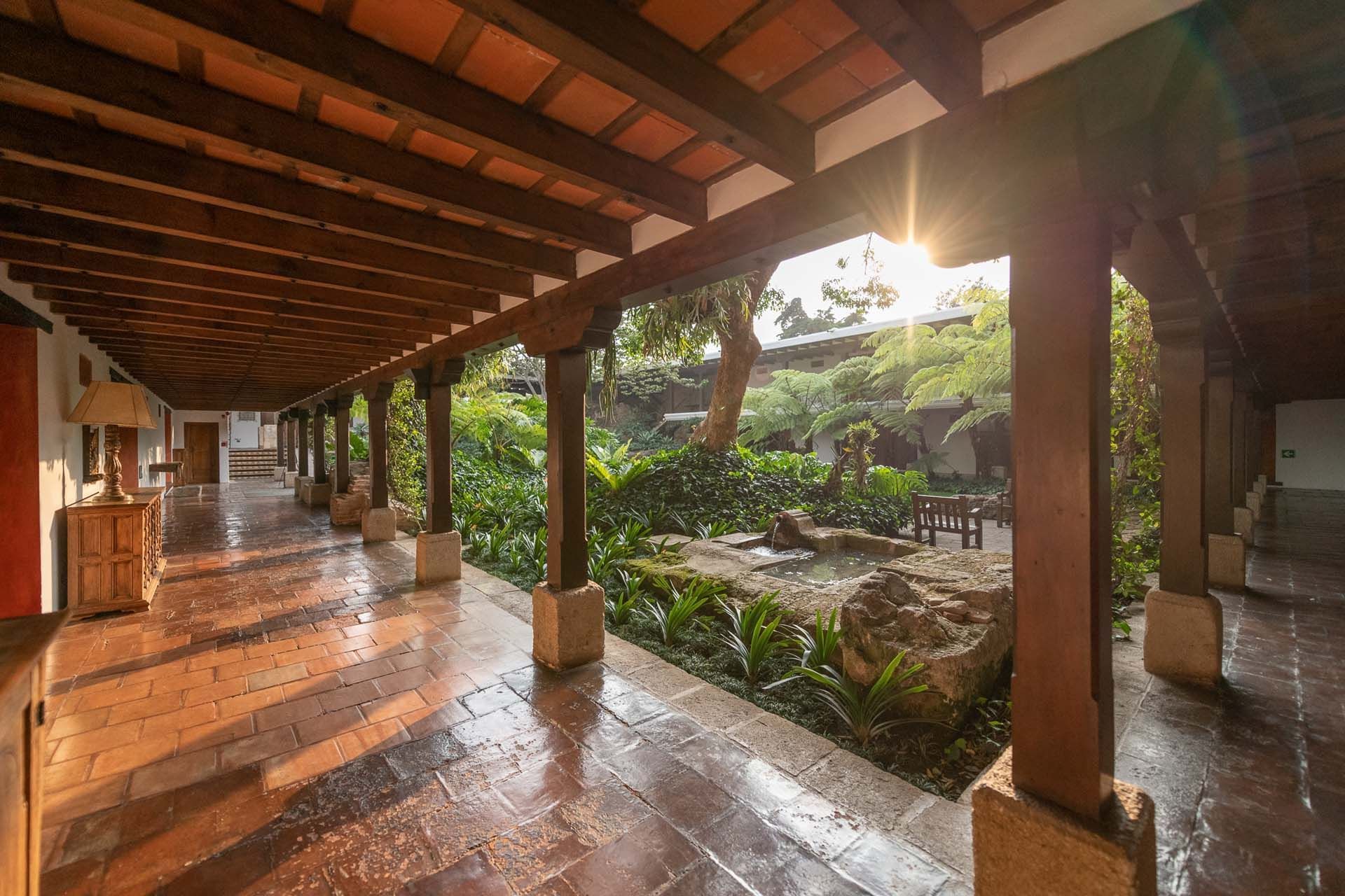Pasillo con columnas junto a un jardín y una fuente bajo un techo con vigas en Casa Santo Domingo