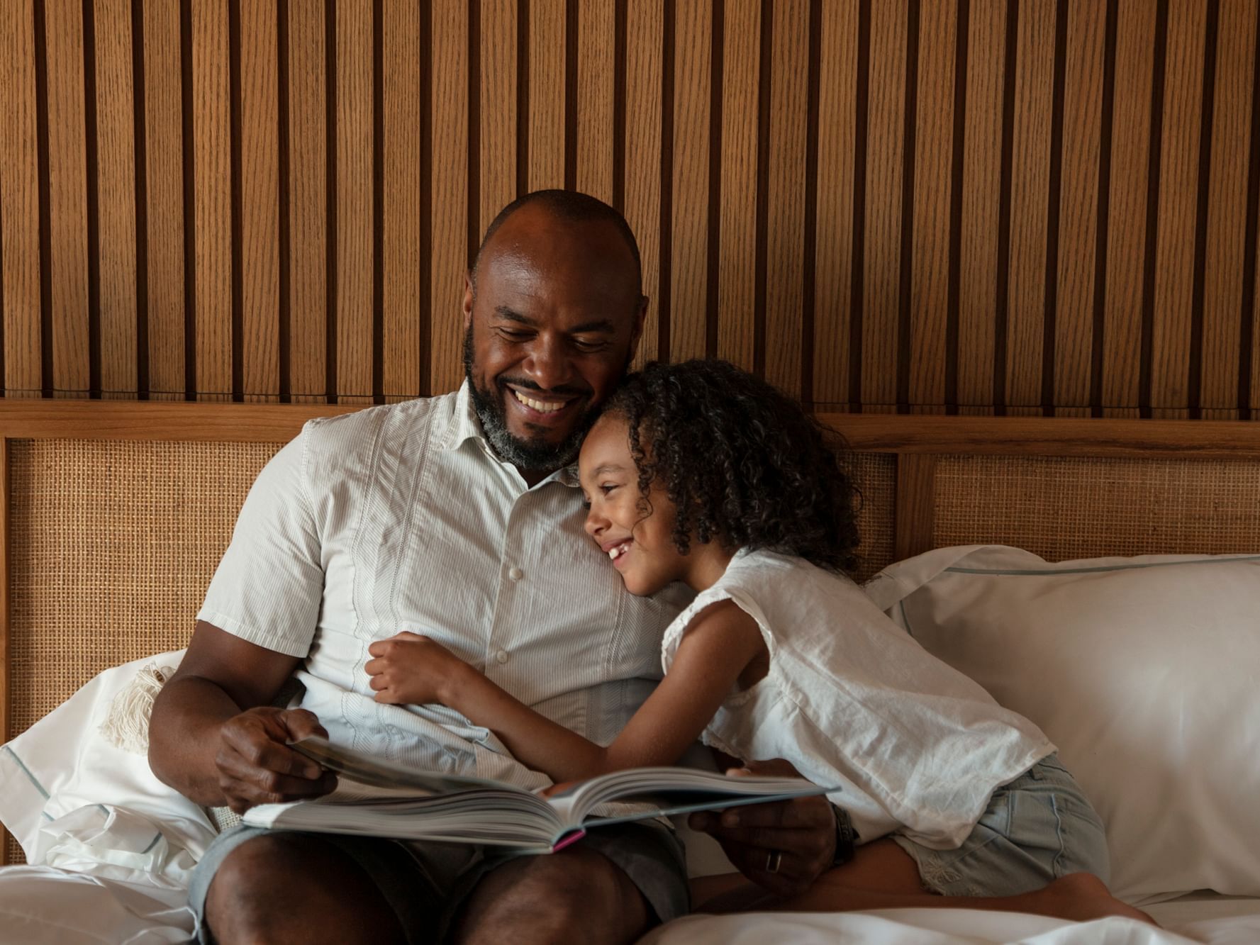 Dad reading a book with kid on bed in room, The Rockaway Hotel