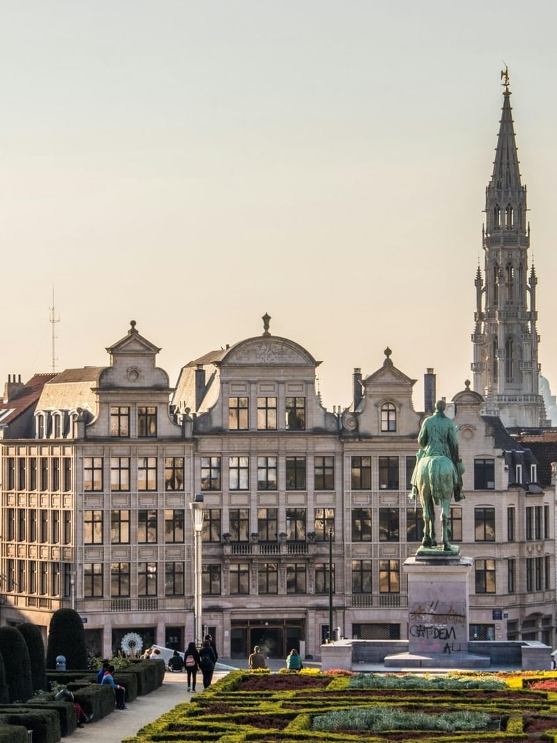Mounted statue by manicured gardens and a tall spire under a golden sunset in Grand Place near Hotel Barsey by Warwick