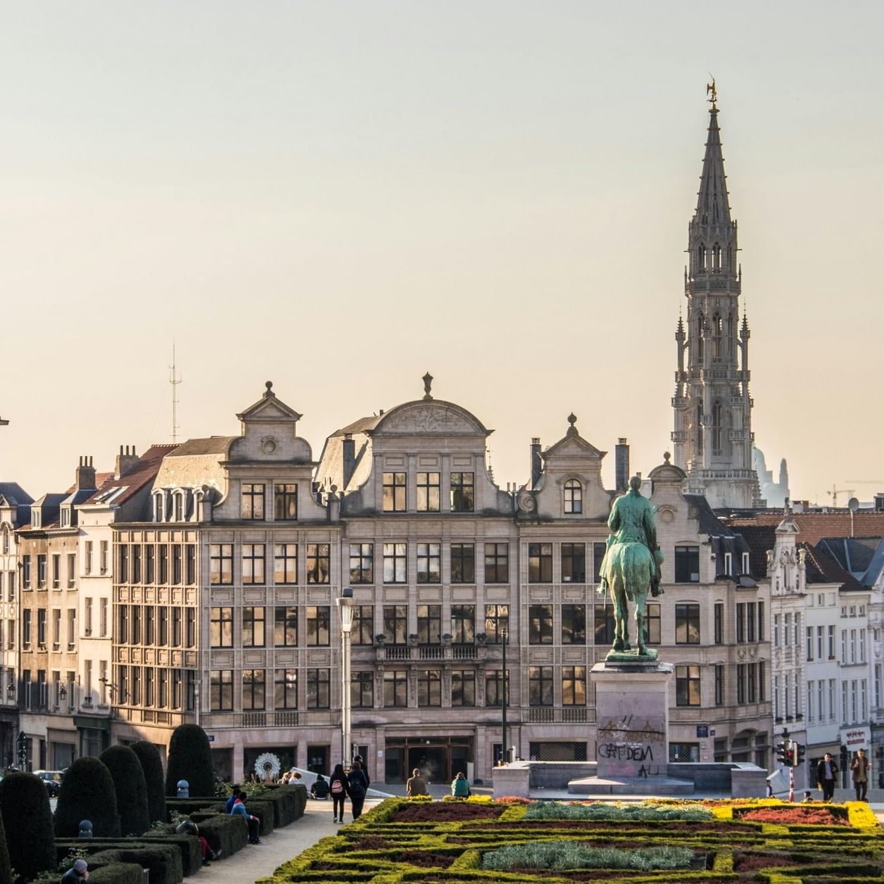 Mounted statue by manicured gardens and a tall spire under a golden sunset in Grand Place near Hotel Barsey by Warwick