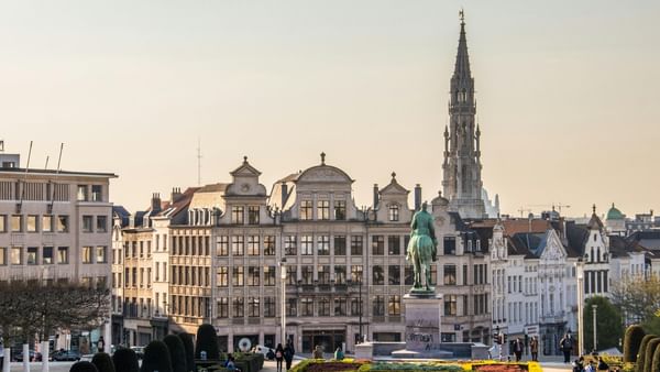 Mounted statue by manicured gardens and a tall spire under a golden sunset in Grand Place near Hotel Barsey by Warwick