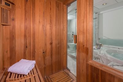 Sauna with a towel on the wooden bench and a glass door leading to the marble bathroom at Hotel Los Delfines & Casino