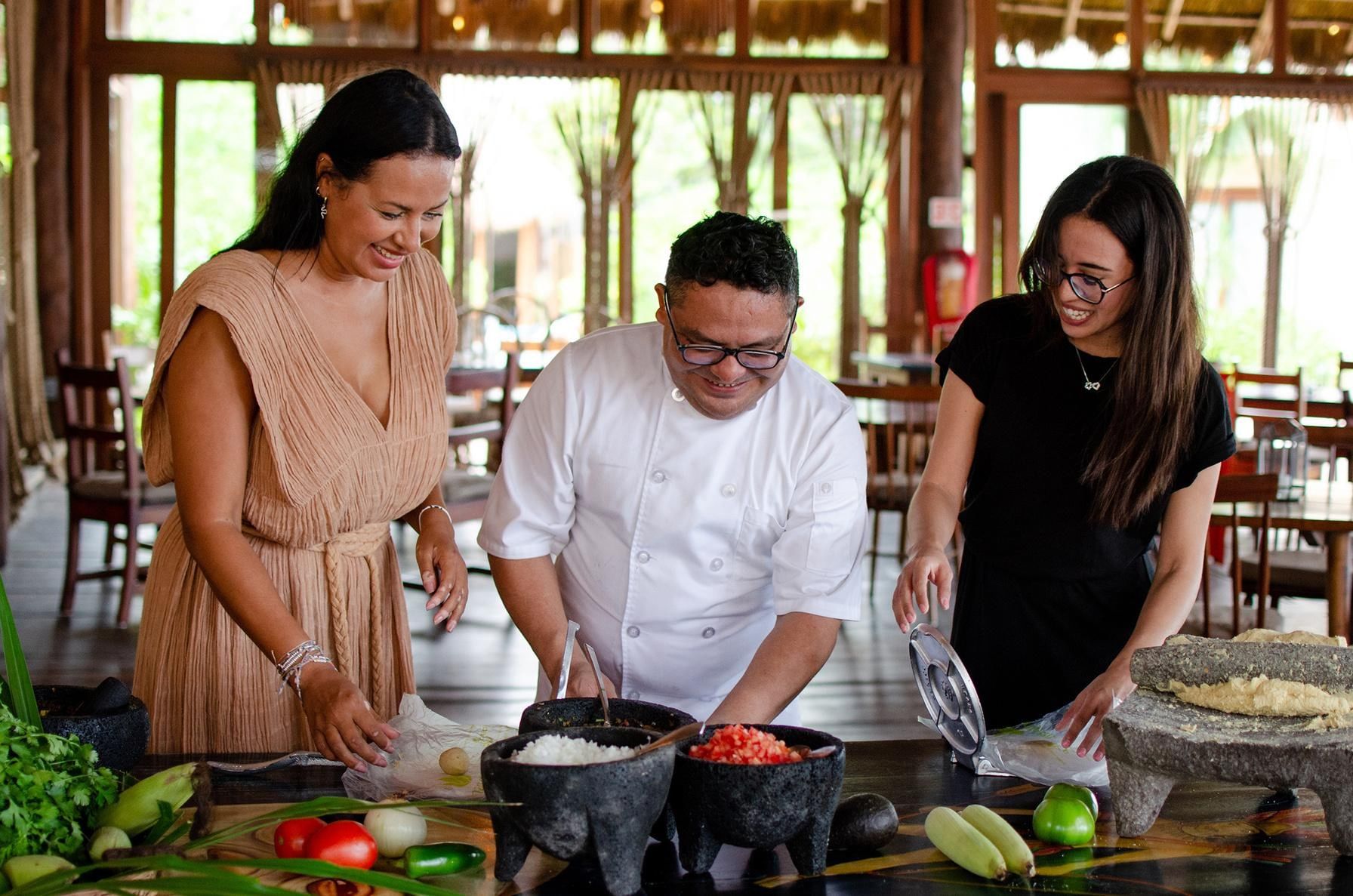 A chef and two guests preparing tortillas and salsa together at La Zebra