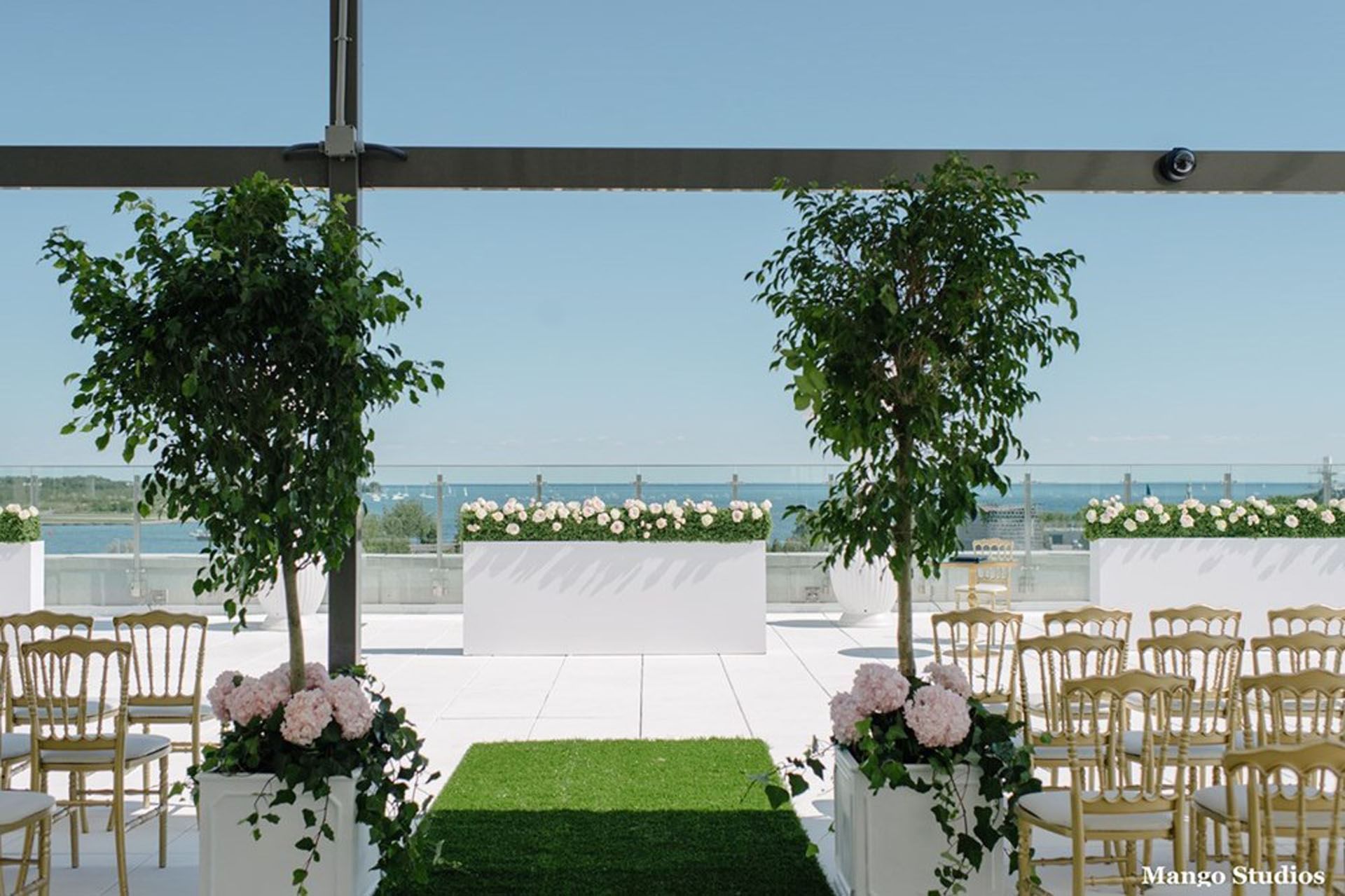 Outdoor terrace on High Park Terrace with gold chairs and white flower arrangements facing water view at Hotel X Toronto