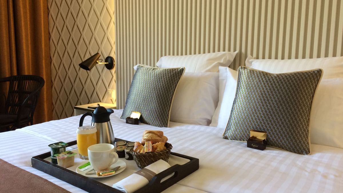 Lit avec plateau de petit-déjeuner, tasses, jus, viennoiseries et théière.