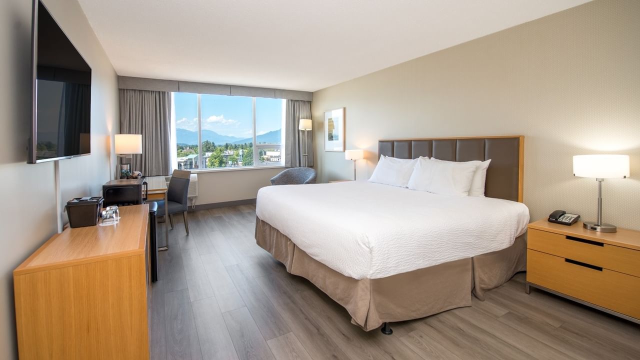 A hotel room with a large bed, flat-screen TV, and a large window.