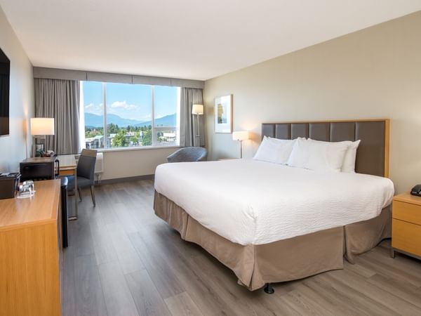 Accessible hotel room with a king bed, nightstands, desk, chairs, large window, and TV on the wall.