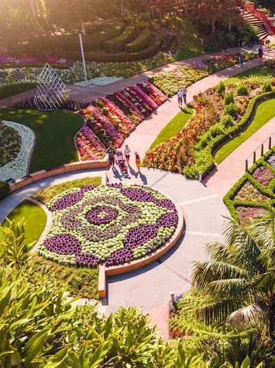 Aerial view of Roma Parkland featuring colorful floral displays, curved pathways, manicured gardens, and a pond.