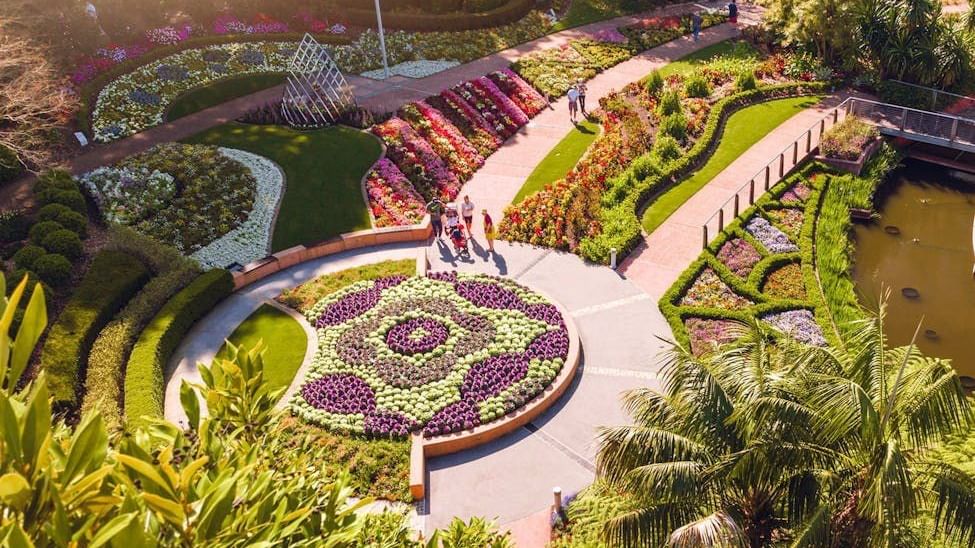 Aerial view of Roma Parkland featuring colorful floral displays, curved pathways, manicured gardens, and a pond.