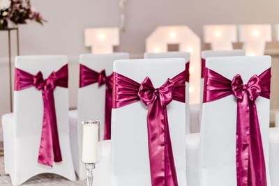 White covered chairs with fuchsia ribbons at a wedding ceremony at The Aberdeen Altens Hotel