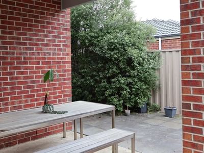 Wooden table with potted plant and bench against brick wall at La Trobe University Regional Housing - Ballarat.