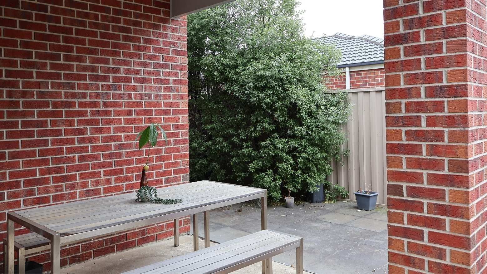 Wooden table with potted plant and bench against brick wall at La Trobe University Regional Housing - Ballarat.
