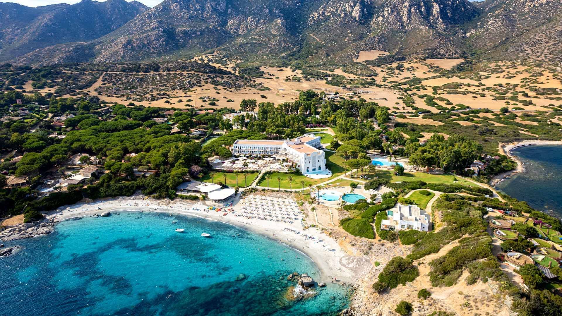 Aerial view of Falkensteiner Resort Capo Boi with a sea and mountain backdrop