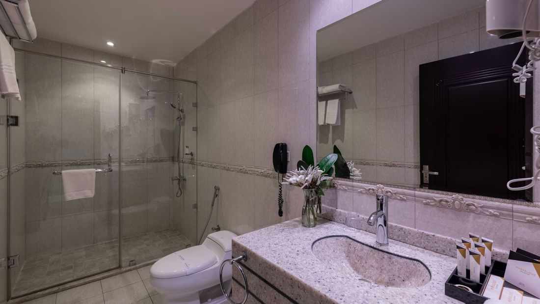 Granite vanity by a white toilet & a glass shower with a towel on handle in Family Suite Sea View at Warwick Al Jubail