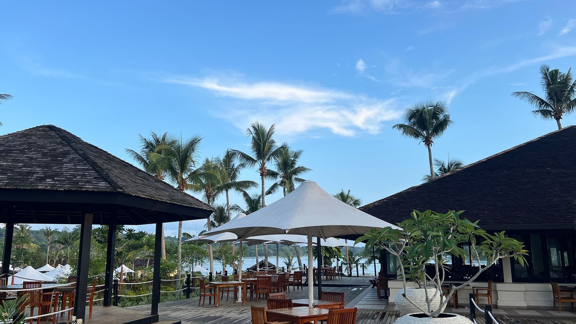 Outdoor dining area with wooden tables and umbrellas at Lagoon Terrace Restaurant in Efate at Warwick Le Lagon