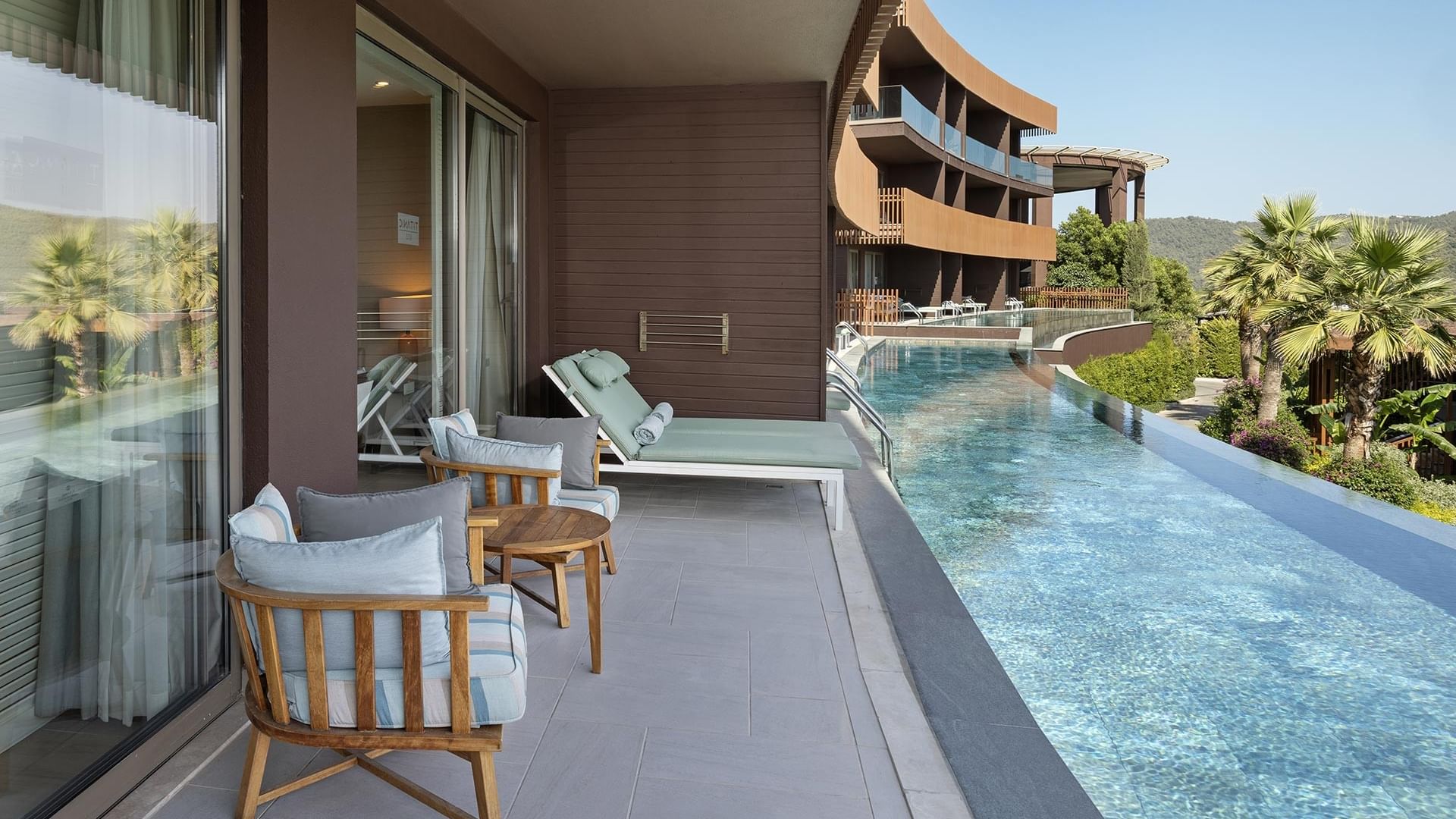 Swim-up Deluxe Room's balcony with lounge chairs, a wooden table at Titanic Luxury Collection Bodrum.