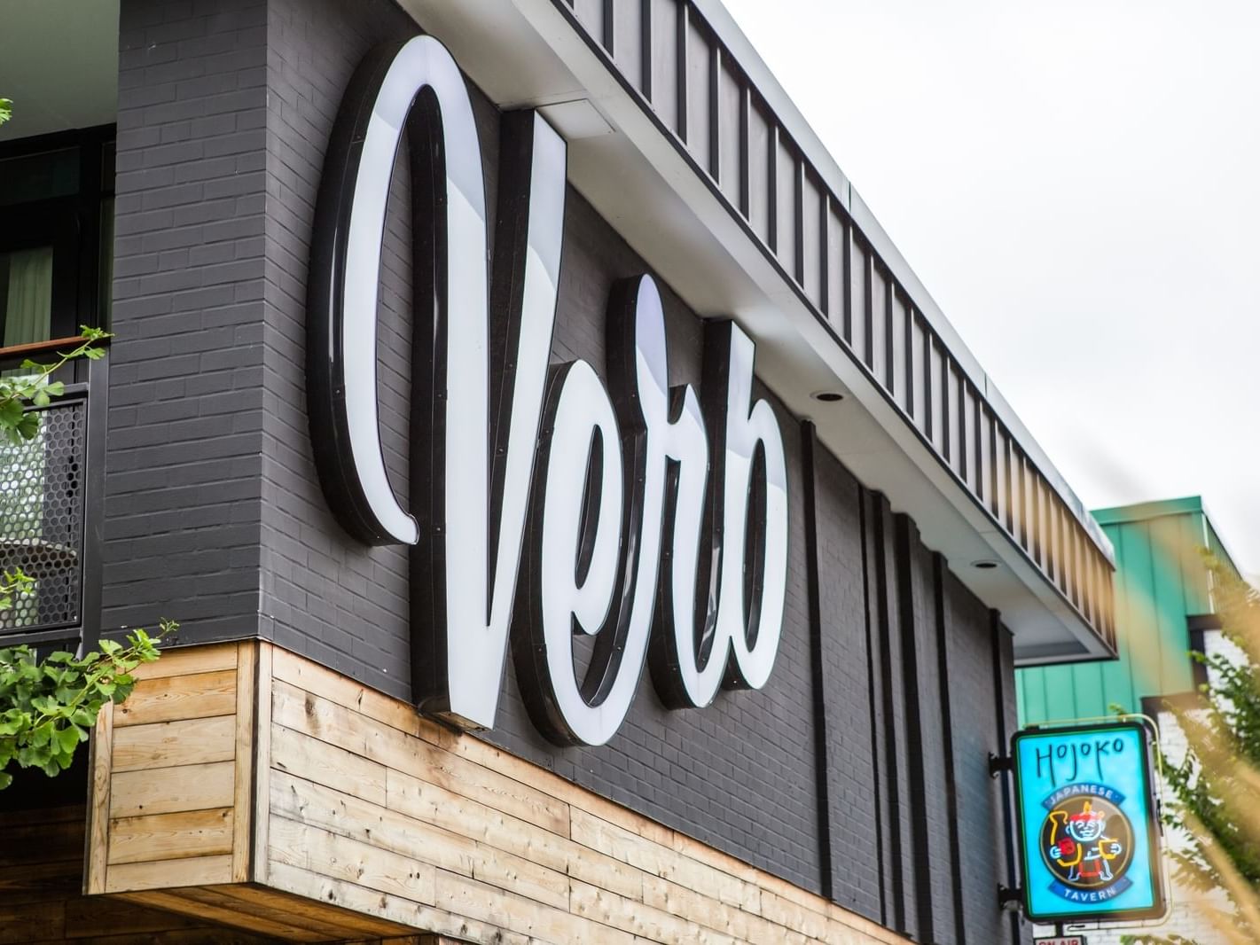Exterior of a Verb-branded building with a balcony and a nearby Japanese tavern sign.