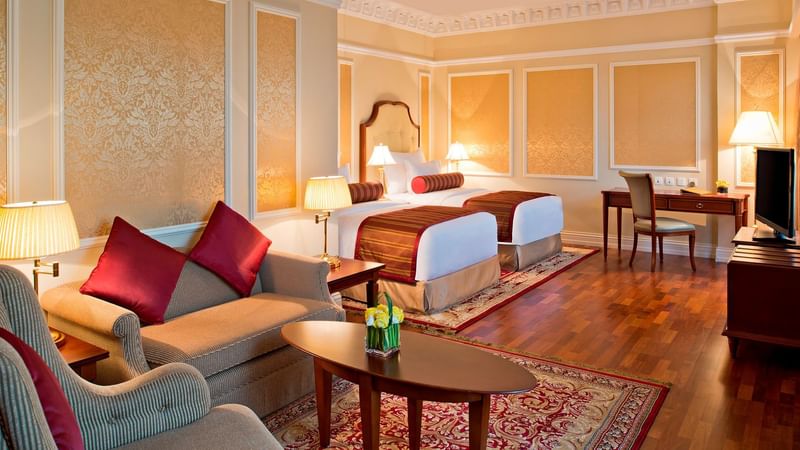 Cozy bedroom featuring double beds & lounge area in Junior Suite at Warwick Doha