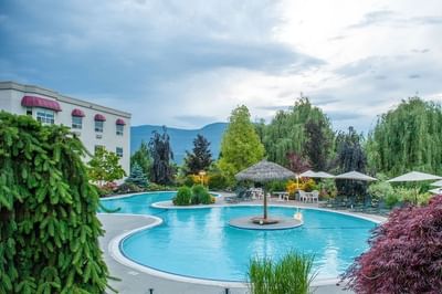Large outdoor pool with swim-up island bar surrounded by lush trees at Hilltop Inn, Salmon Arm 