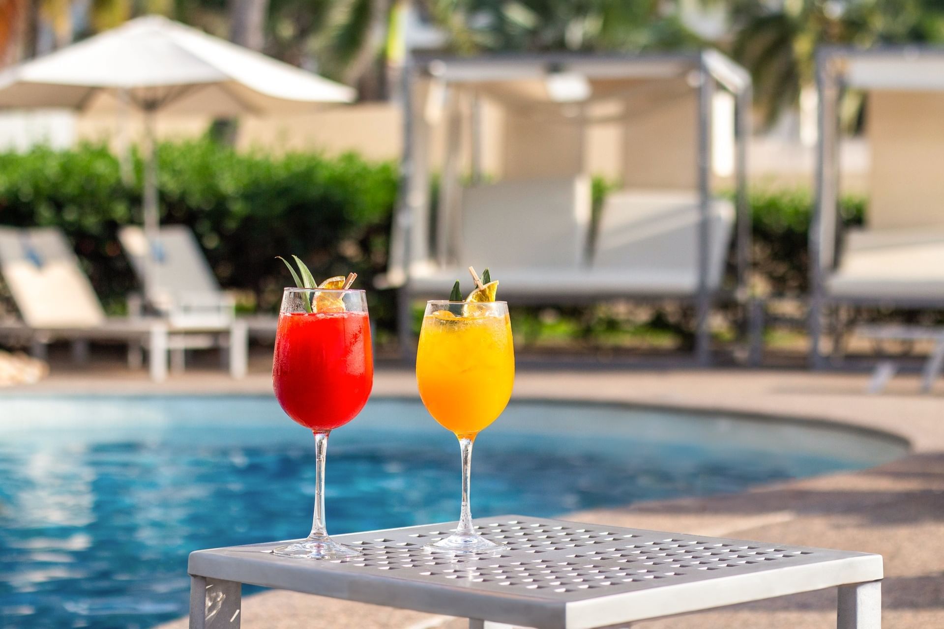 Dos cócteles de colores vibrantes sobre una mesa junto a la piscina con tumbonas en el Sunset Plaza Beach Resort, uno de los mejores hoteles en Puerto Vallarta