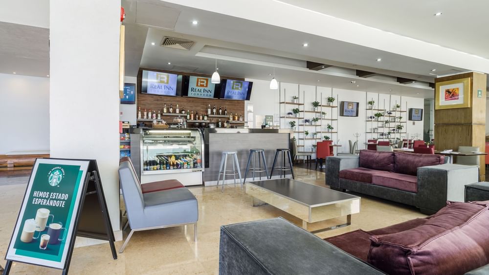 Stylish Kiosko bar with purple velvet sofas, a coffee station, and modern shelving units at Real Inn Torreon
