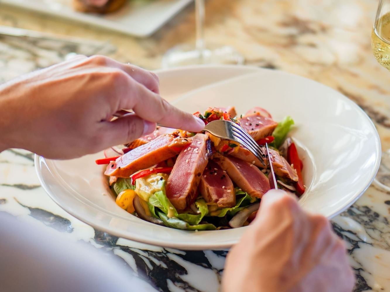 Person enjoying a fresh salad topped with sliced grilled meat and vegetables in the Breeze Restaurant at Golden Rock Resort