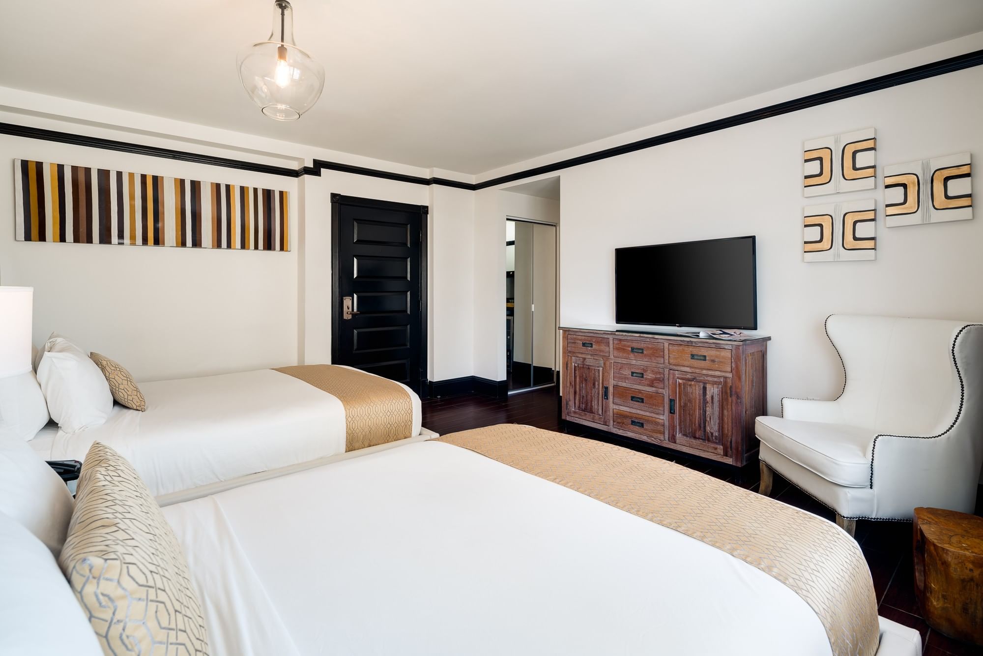 A hotel room with two queen beds, a TV on a dresser, and an accent chair.
