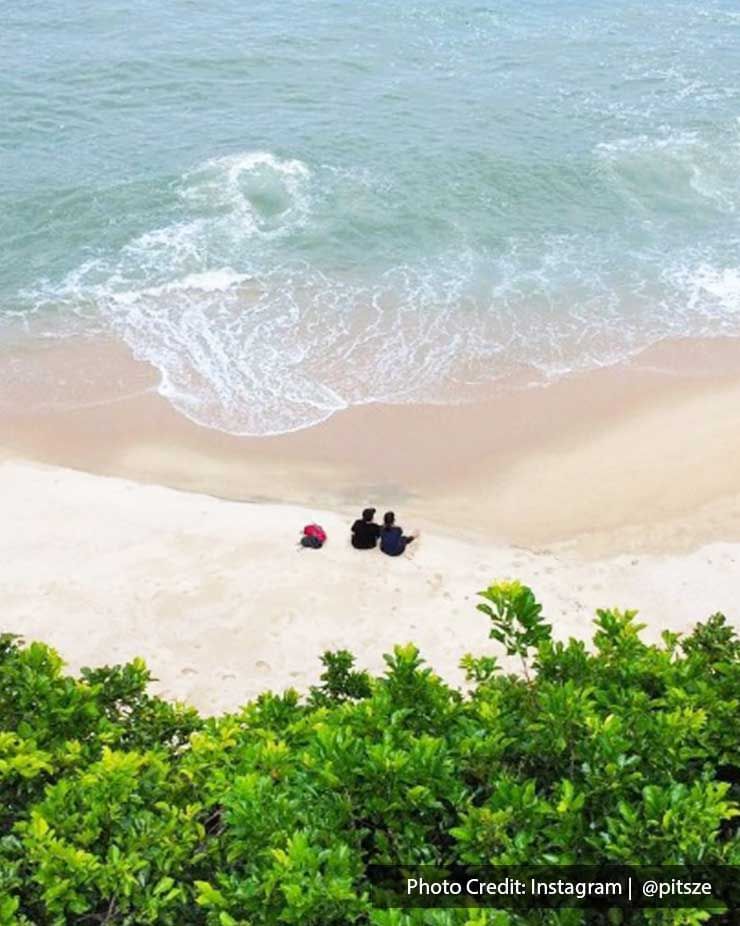 Two people sit on a sandy beach beside the sea at Pantai Kerachut -Lexis Suites Penang