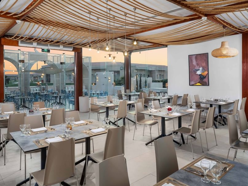 Indoor restaurant with wooden ceiling, large windows, and many tables set with glasses and silverware.